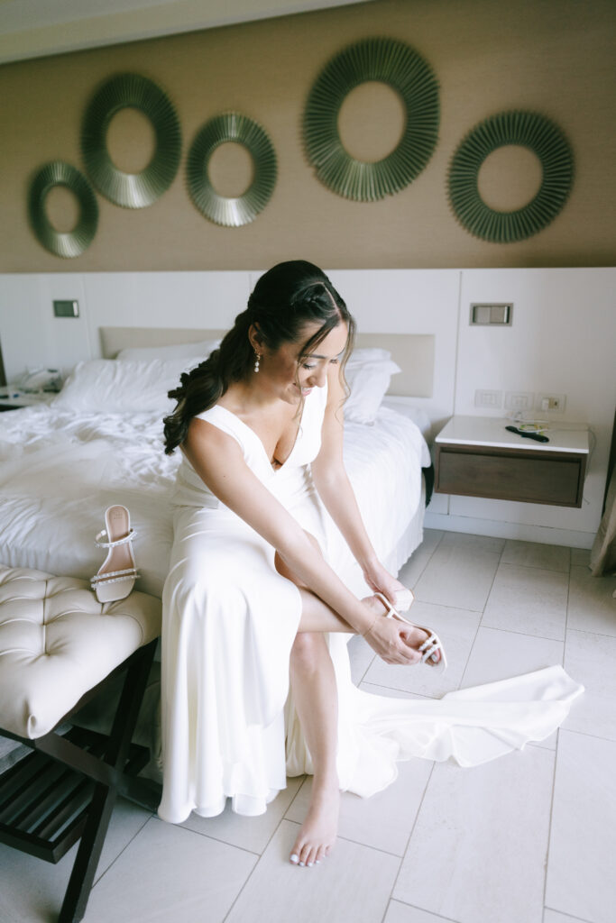 Seated Bride putting on wedding shoes in white wedding dress with green circular mosaic wall art