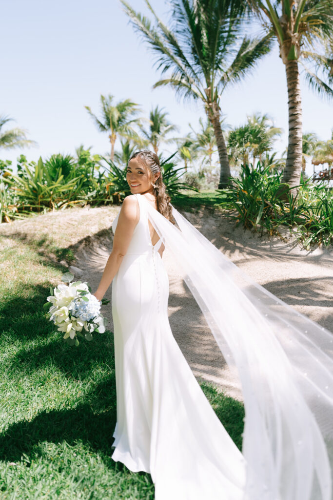 Full body image of Bride looking over her shoulder on a sunny day with lush grass and palm trees