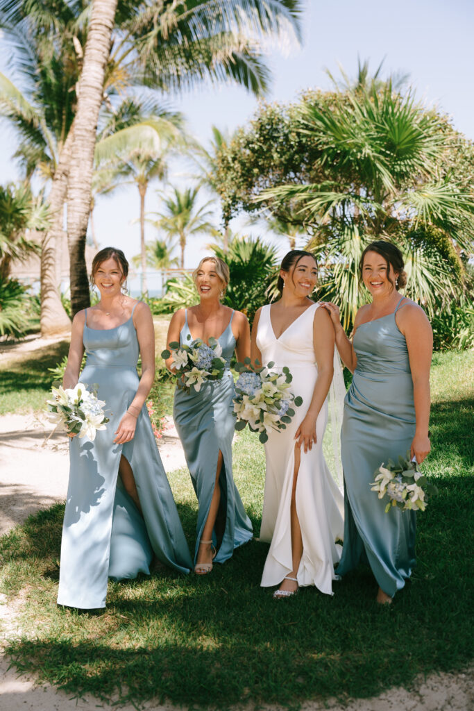 Bride in wedding dress and Bridesmaids in blue dresses with flowers walking and smiling with palm trees in the background