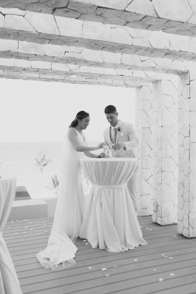 Bride and Groom stand together over a circular table filling sand into a jar.