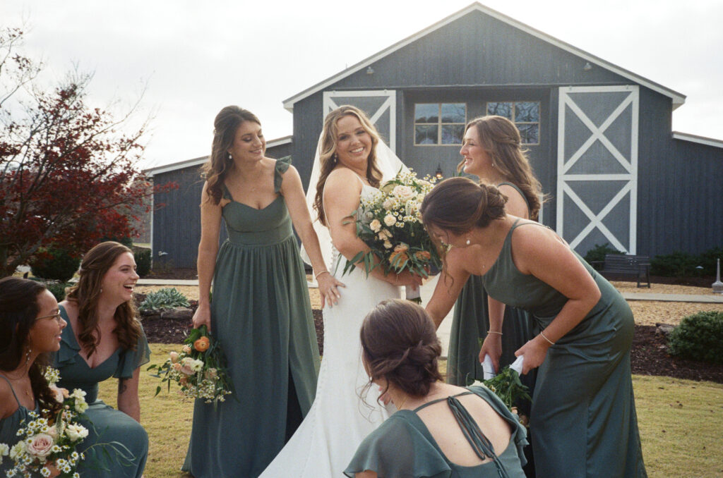 Bride gazes at the viewer while surrounding bridesmaids fluff and fix her gown.