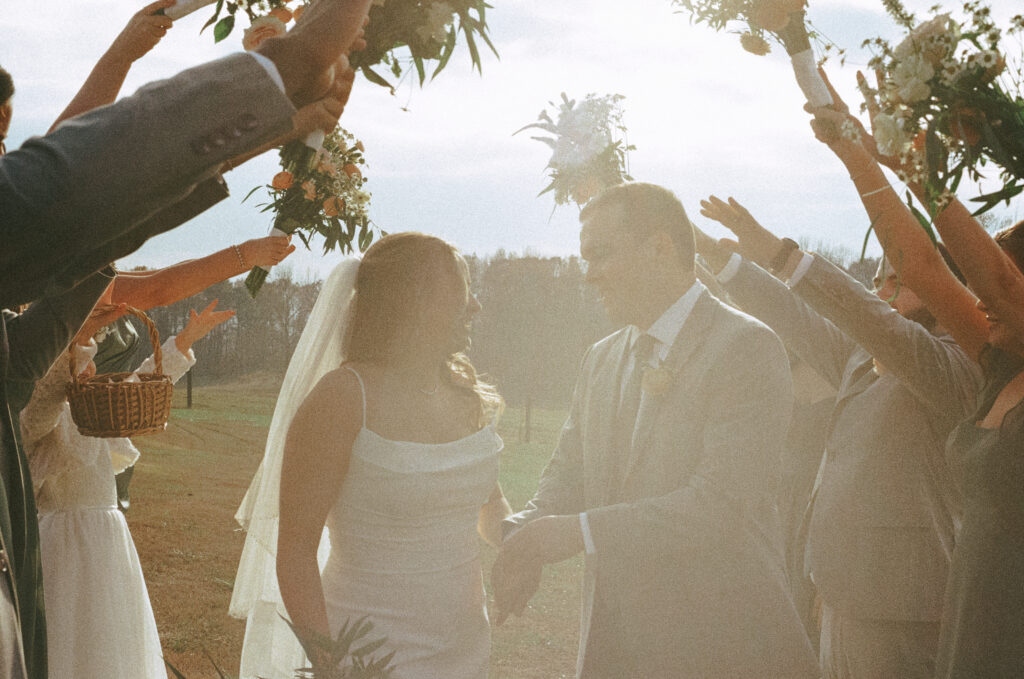 Bride and Groom walk underneath an arch of raised arms of bridesmaids and groomsmen.