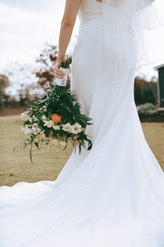 Bouquet of colorful florals held in bride's hand framed by the train of her wedding gown.