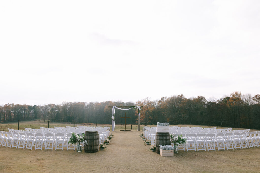 Wedding alter with a large wooden cross and white chairs set up to either side creating an aisle.