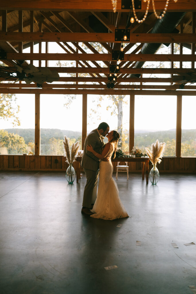 Bride and Groom embrace in a dance with wooden beams and a concrete floor. Floor to ceiling windows show a mountain view in the background.