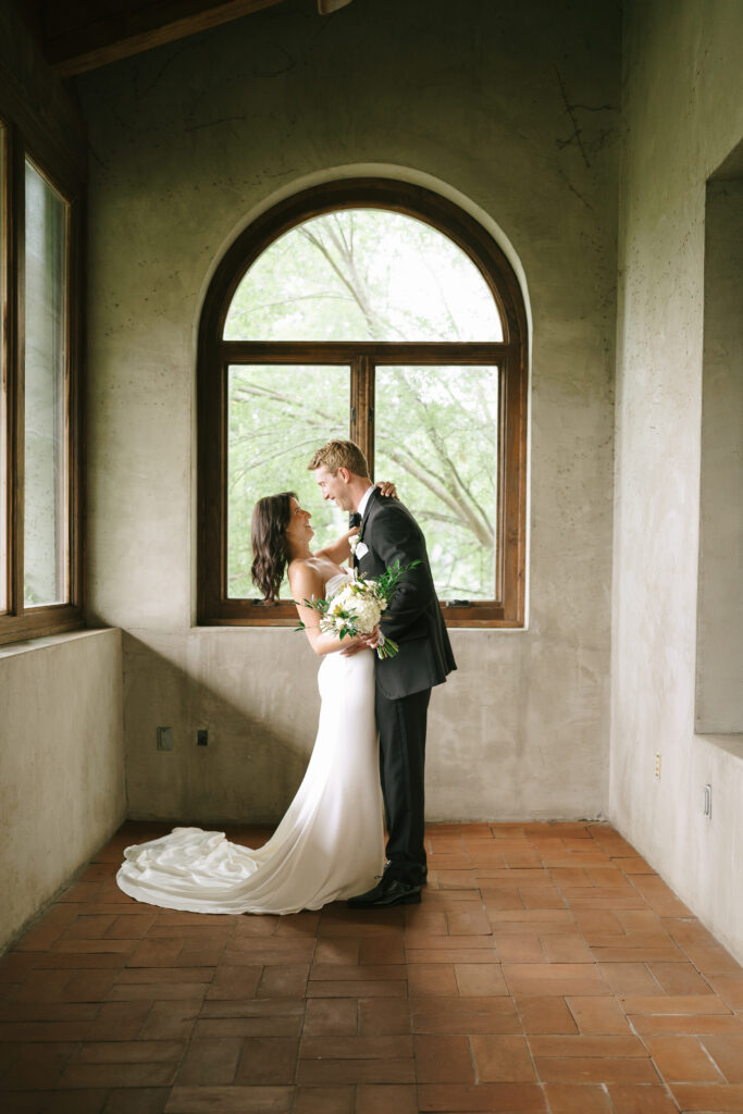 Groom and Bride embrace framed by an arched wooden window.