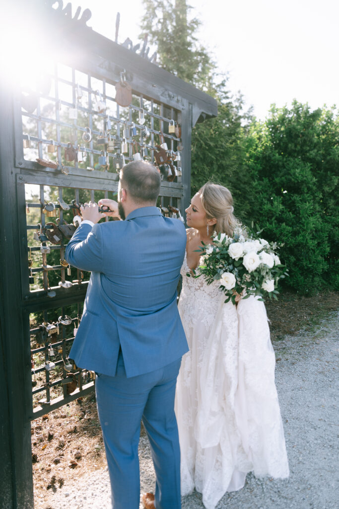 Bride and Groom stand in front of a rectangular lattice filled with locks, securing a lock. 