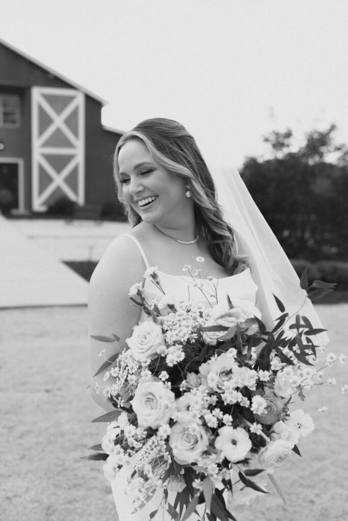 Black and white photo of a bride laughing over her shoulder holding a large bouquet of flowers.