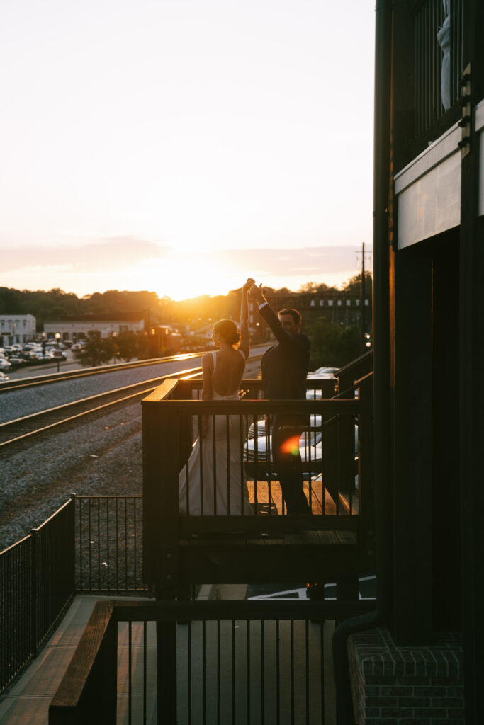 Groom spins bride on a metal balcony at the Cowan Historic Mill as the sun sets in the background.