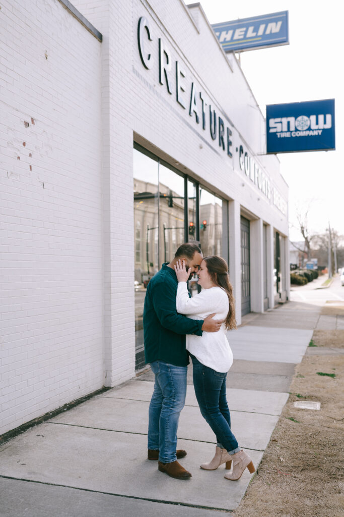 Couple standing and embracing on the sidewalk in front of the white brick Creature Comforts brewery