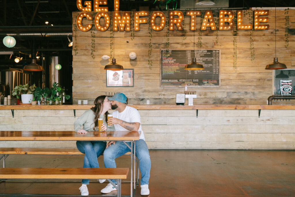 Couple sitting and kissing at a picnic table inside Creature Comforts Brewery