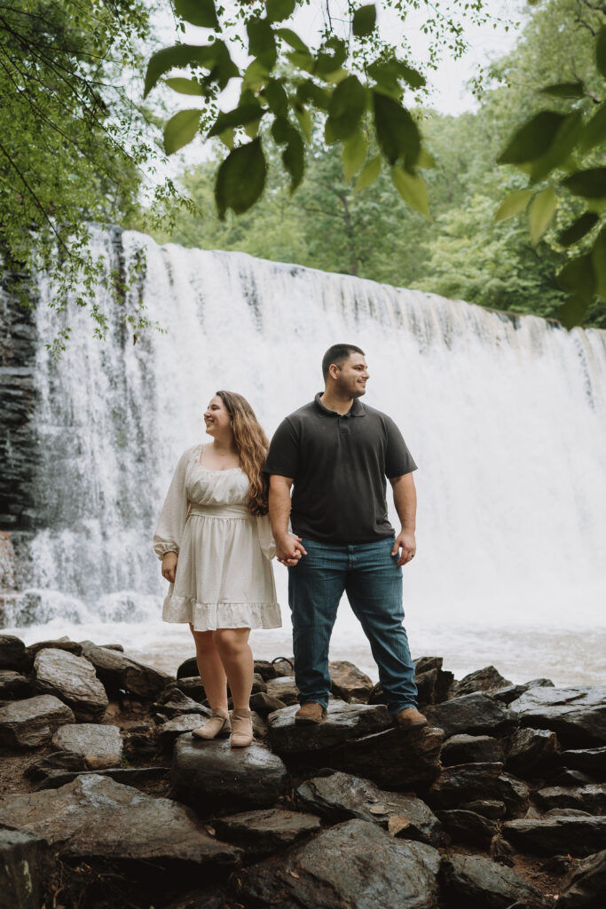 Couple standing hand in hand in front of a waterfall at The Roswell Mill