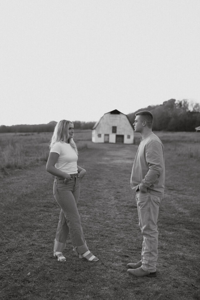 Couple standing in front of a white barn in a field at Vaughters Farm