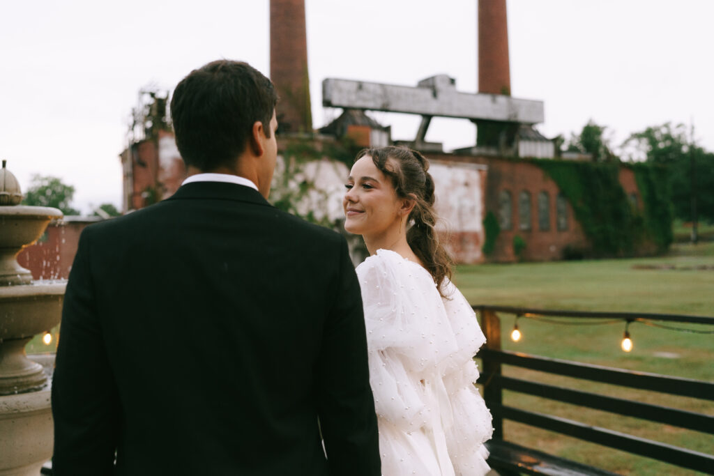 Close up of Bride gazing to the left at her groom. An old, ivy covered brick mill with two large stack houses in the background.