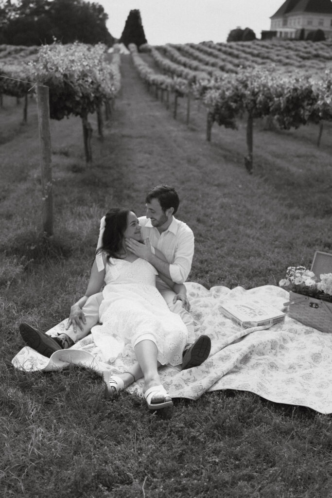 In black and white of a couple lounging on a picnic blanket between rows of grape vines at Chateau Elan