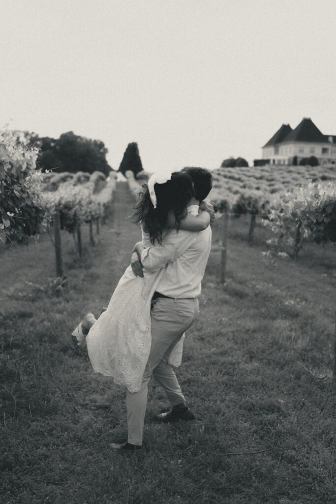 In black and white of man swinging woman, embracing, between rows of grape vines at Chateau Elan