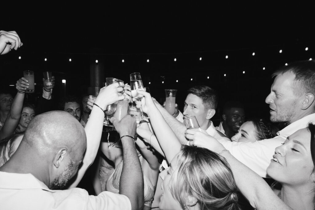 Bride, Groom, family and friends toasting with glasses and smiling.