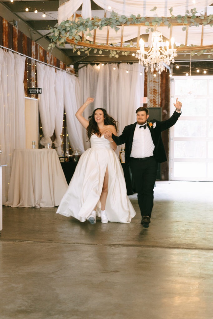 Bride and groom dancing and waving arms entering their reception.