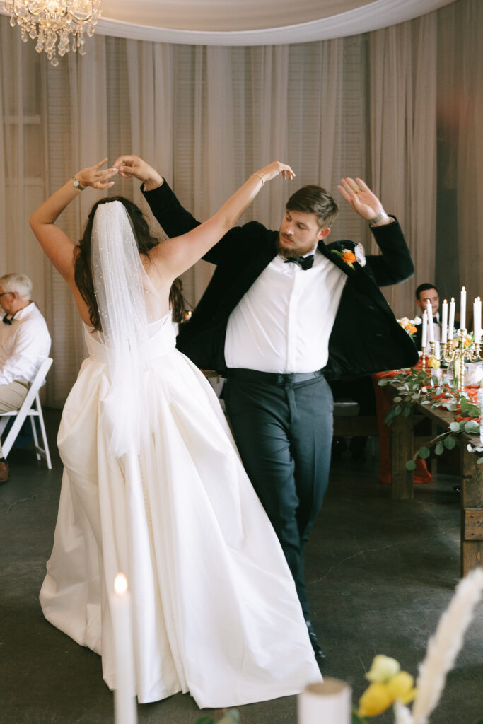 Bride and groom dancing with arms raised.