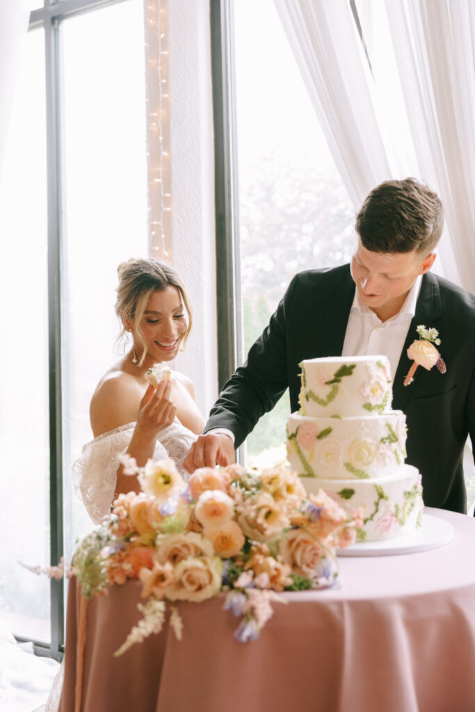 Bride and Groom smiling and tasting a three tiered floral patterned cake