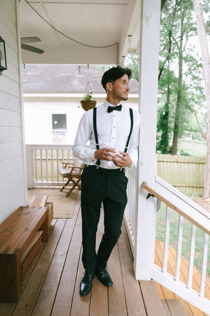 Groom in a black and white tuxedo staring over his shoulder on a porch.