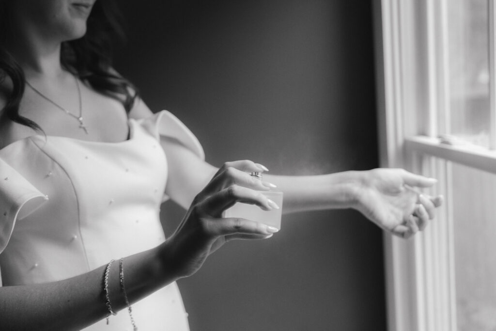 In black and white of bride spraying perfume onto wrist.