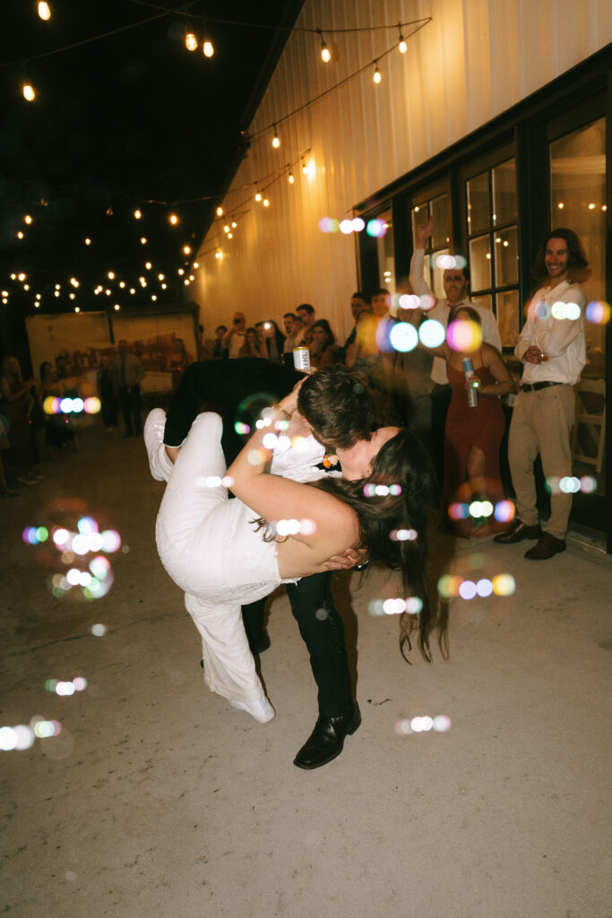 Groom dipping bride for a kiss with multicolored bubbles floating in the air.