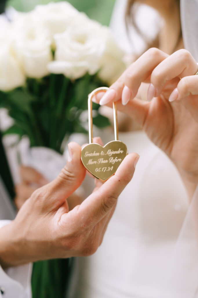 Bride and groom holding a gold heart shaped lock with their names and wedding date engraved.