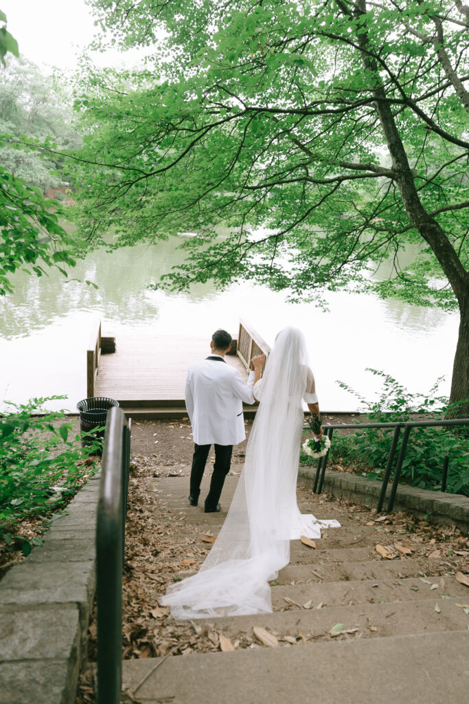 Groom helping bride down stairs towards wooden dock in Piedmont Park.