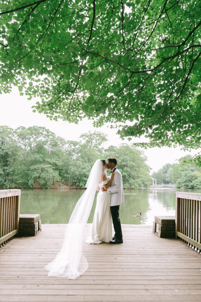 Bride and groom standing on a dock in Piedmont Park embracing and kissing.