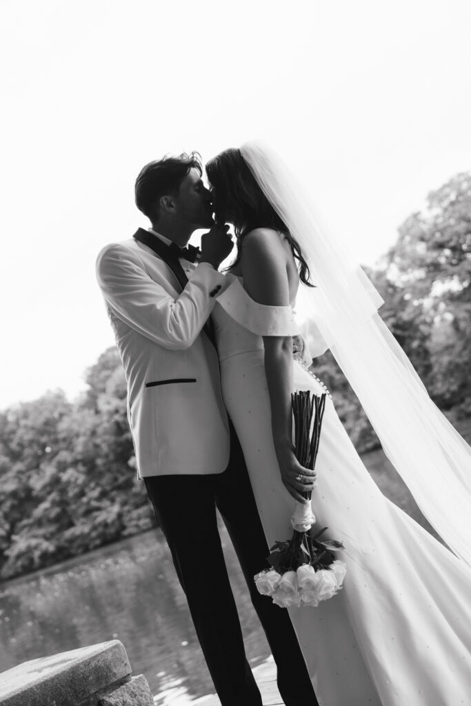 In black and white of groom kissing bride while cupping chin.