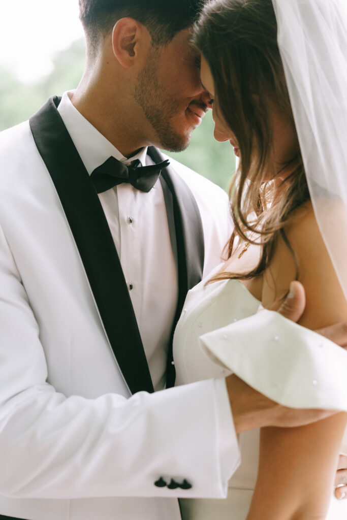 Groom and bride touching foreheads while groom caresses bride's shoulder.