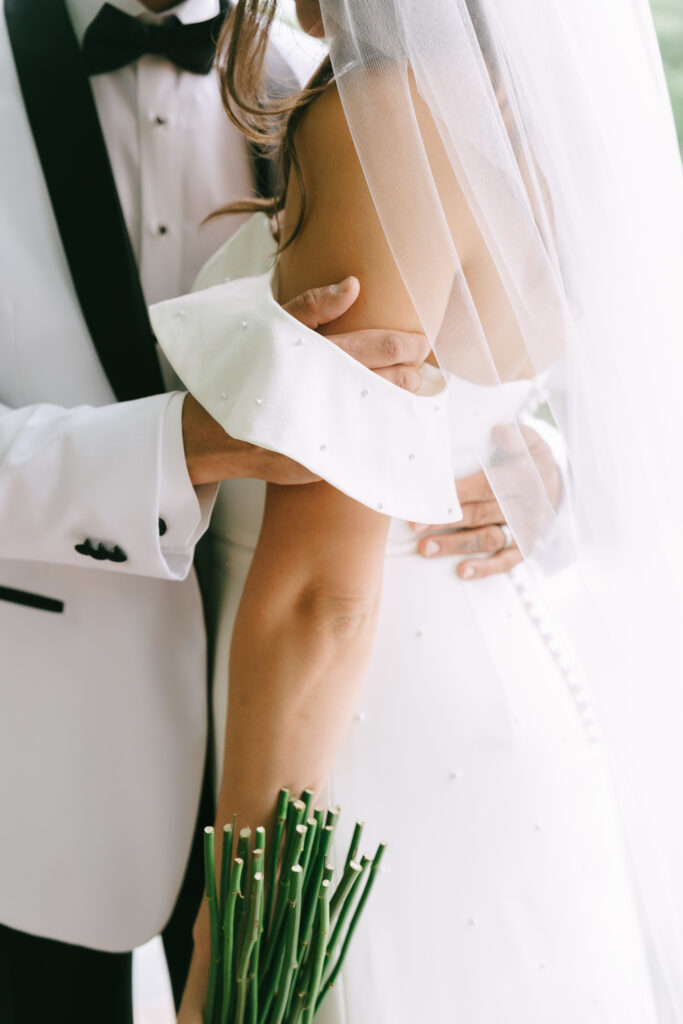 Groom caressing bride's arm underneath off the shoulder bridal gown strap.