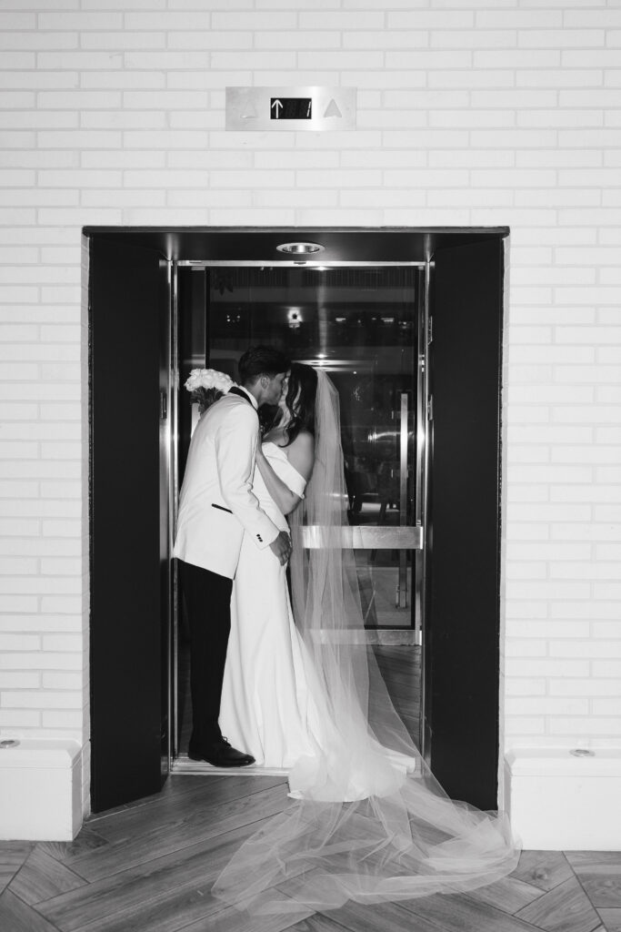 In black and white of bride and groom kissing in an elevator.