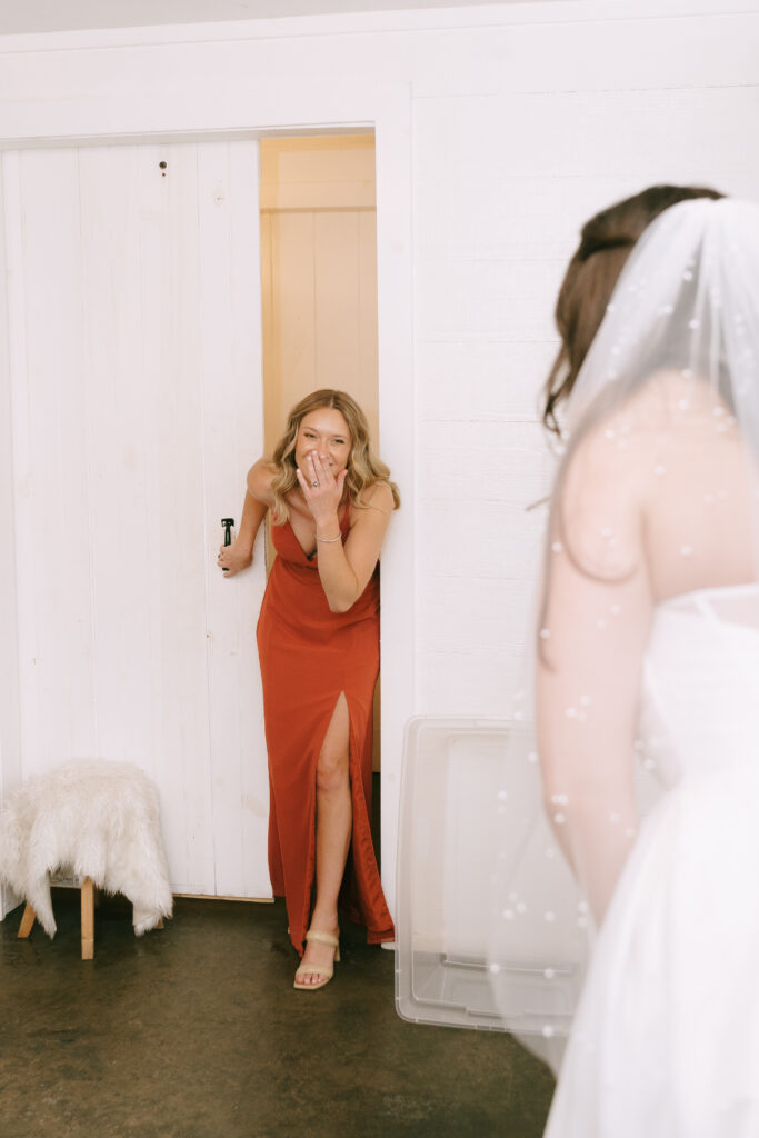 Bridesmaid in an orange dress entering room and seeing bride.