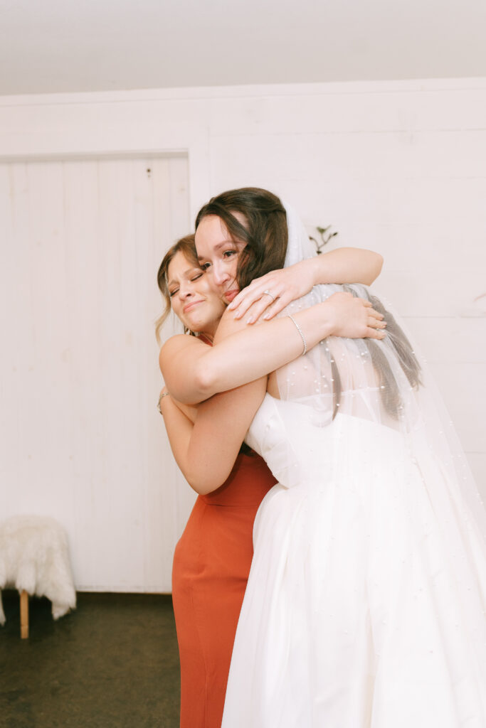 Bridesmaid in an orange dress hugging bride.