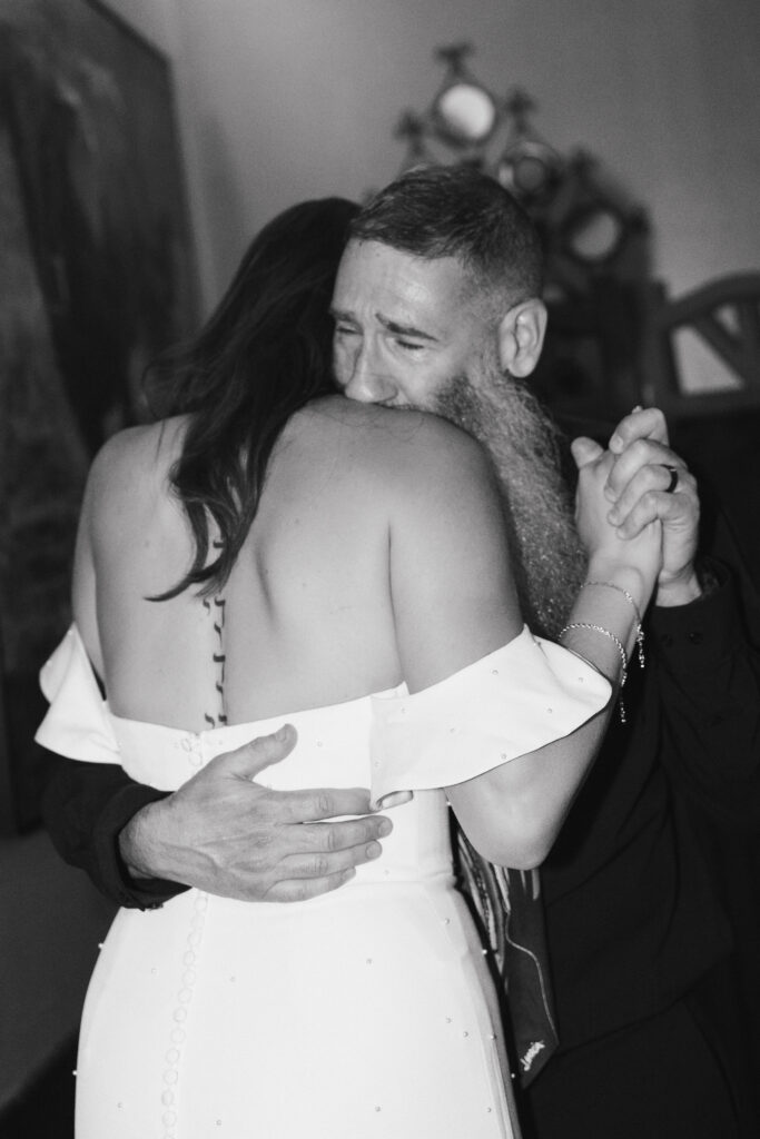 In black and white of bride and her emotional father dancing together at wedding reception.