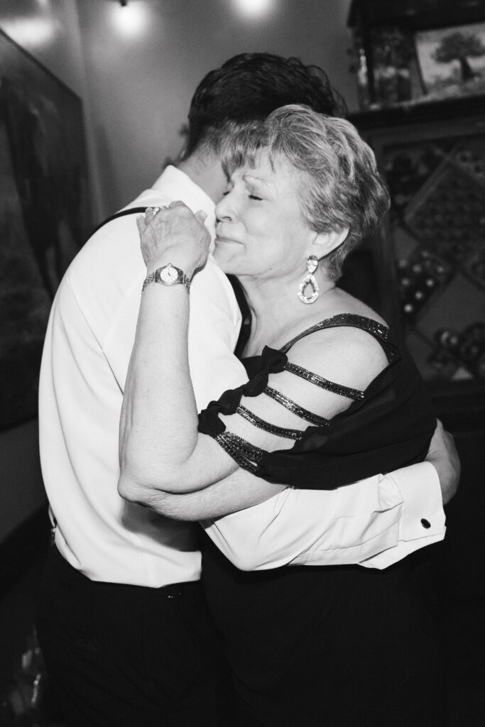 In black and white of groom and his emotional mother dancing together at wedding reception.