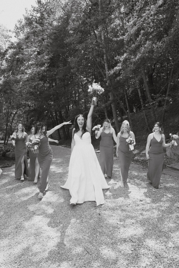 In black and white with bride walking holding up bouquet and bridesmaids walking and cheering behind.