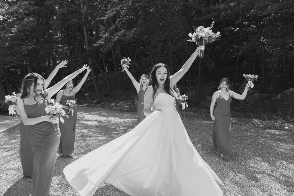 In black in white with bride spinning in a circle with arms raised and bridesmaids cheering.