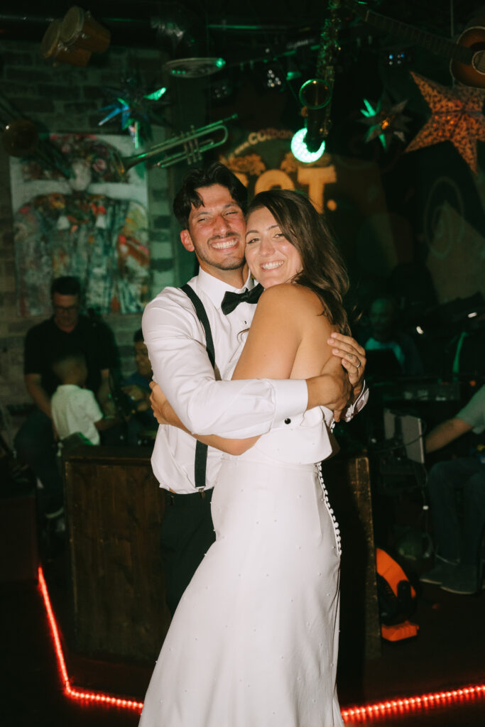 Bride and groom grinning and embracing at wedding reception.