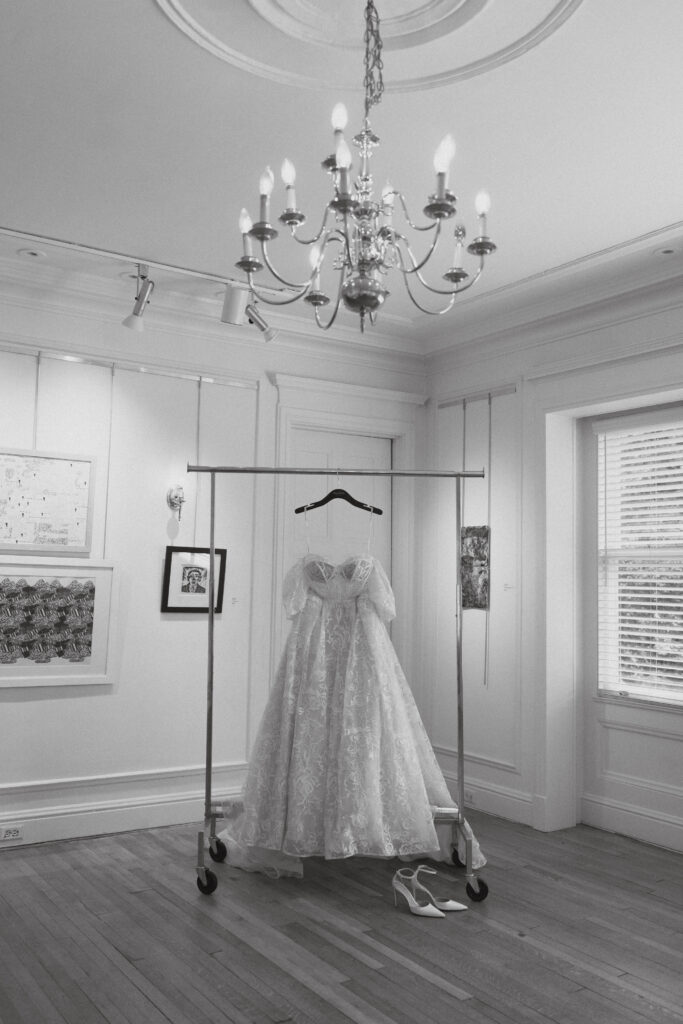 A-line wedding dress hanging in a white walled room with chandelier overhead