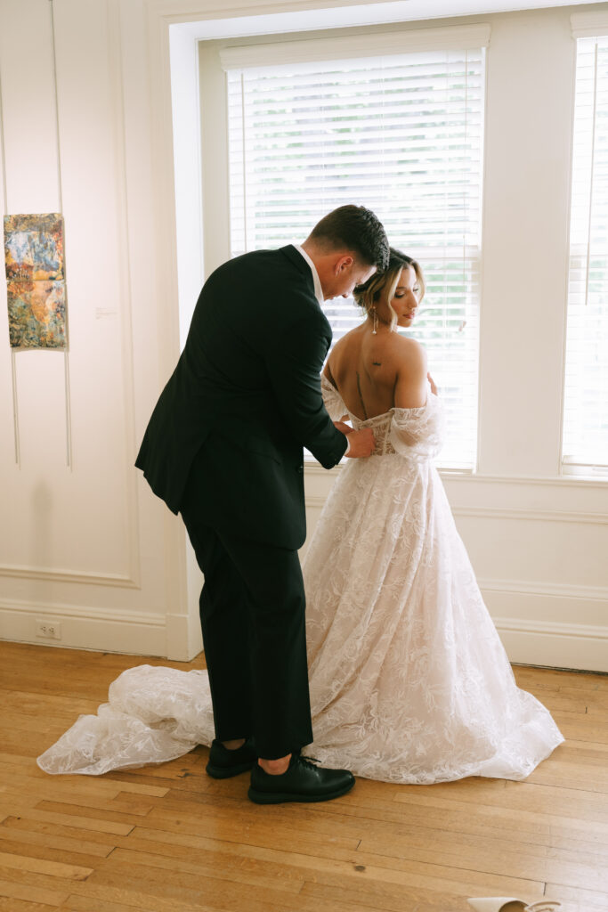 Groom zipping bride into wedding dress