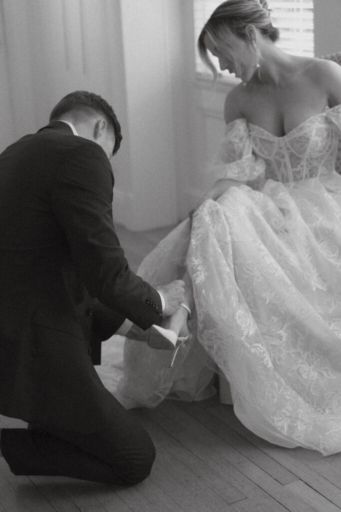 Groom helping bride put on wedding heels