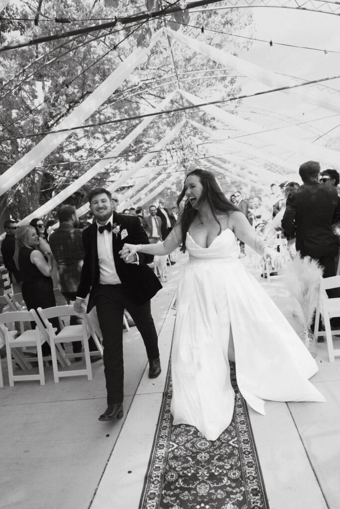 In black and white of bride and groom holding hands walking down the aisle.