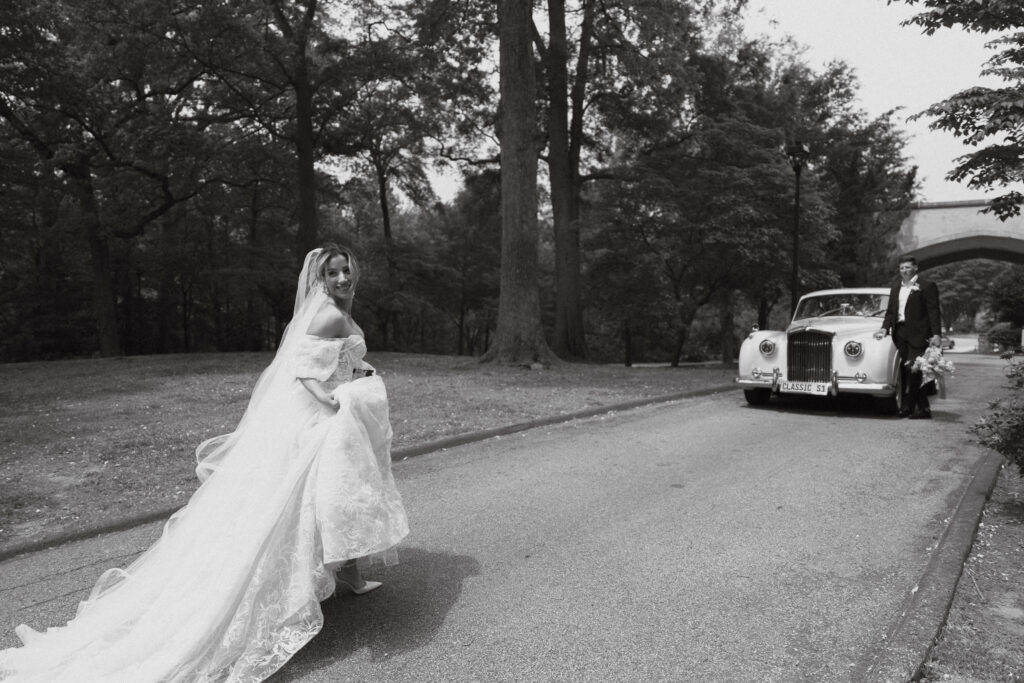 Bride holding dress, skipping towards groom and a while Rolls-Royce